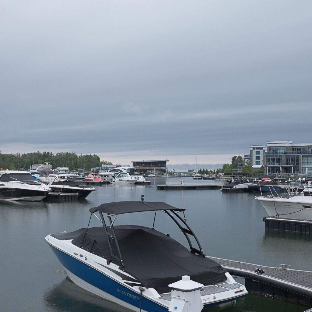 A modern luxury marina boardwalk at Friday Harbour Resort in Innisfil, Ontario, featuring docked boats, sleek lakeside condos, and contemporary boardwalk shops.
