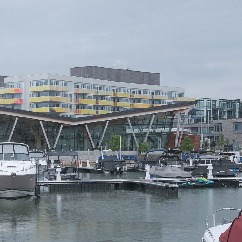 A modern luxury marina boardwalk at Friday Harbour Resort in Innisfil, Ontario, featuring docked boats, sleek lakeside condos, and contemporary boardwalk shops.