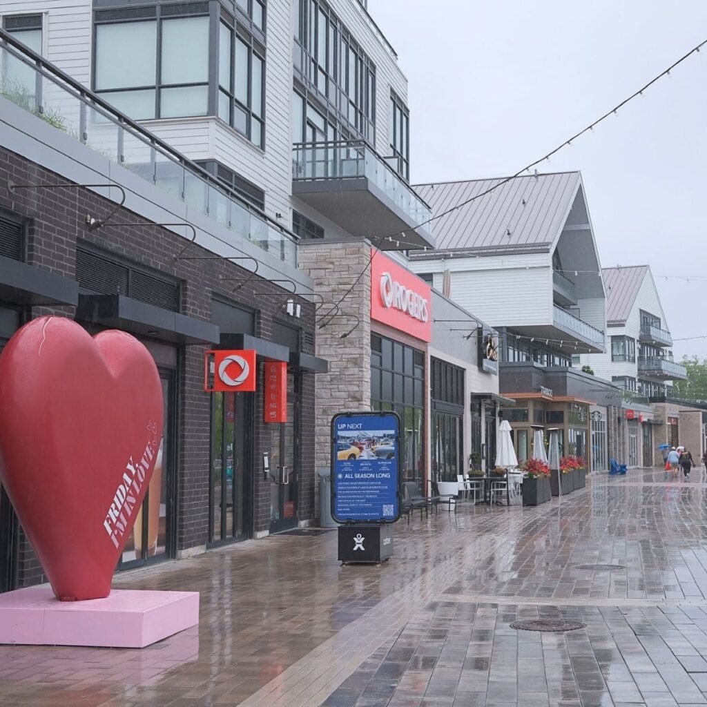 Contemporary boutique shops and restaurants along the boardwalk at Friday Harbour Resort on a rainy day, featuring clean modern architecture and a wet walking path.