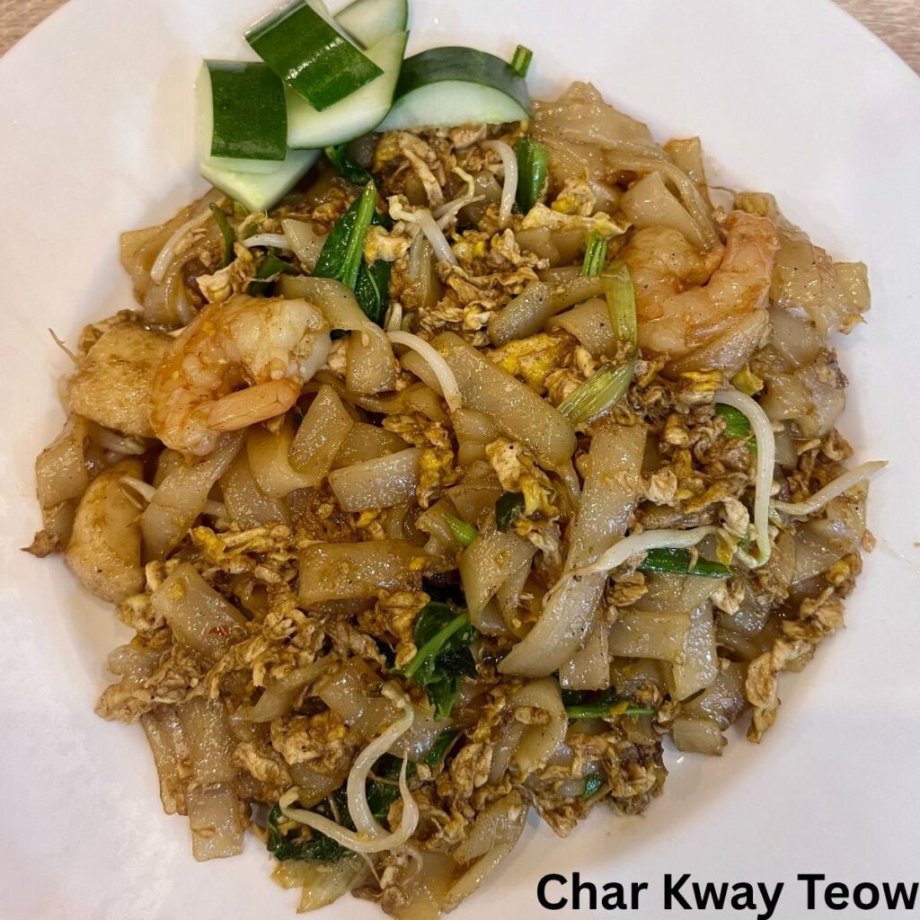 A plate of smoky Malaysian Char Kway Teow, featuring stir-fried flat rice noodles tossed with succulent juicy prawns, bean sprouts, and chives.