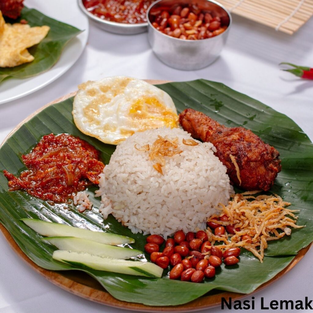 A traditional plate of Malaysian Nasi Lemak served on a green banana leaf, featuring fragrant coconut rice, a crispy fried chicken drumstick, spicy sambal, fried egg, and sliced cucumbers