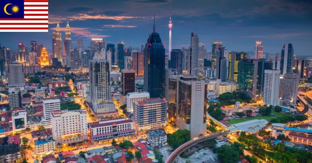 A spectacular dusk skyline view of Kuala Lumpur, Malaysia, featuring the glowing golden lights of the Petronas Twin Towers and iconic city landmarks illuminated against a twilight sky.