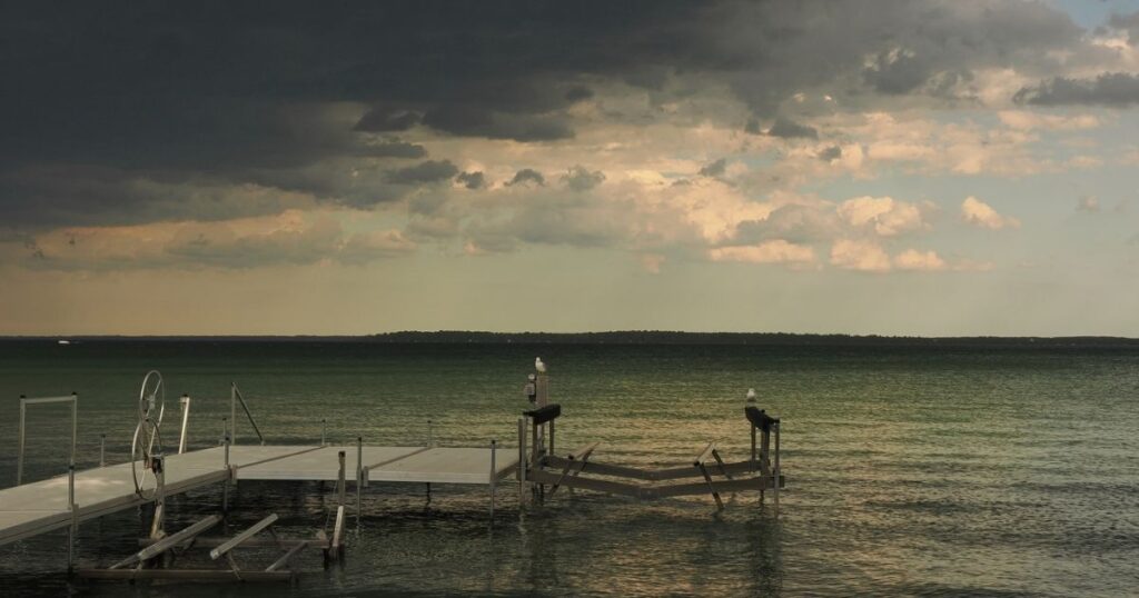 A dramatic, breathtaking view of Lake Simcoe in Innisfil, Ontario, showing calm water shifting colours right before a summer rainstorm rolls in, taken from a private dock.