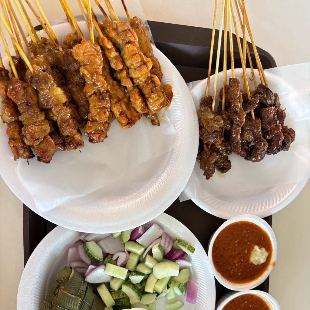close-up food photo of perfectly grilled local Singaporean satay meat skewers served with a rich peanut dipping sauce.