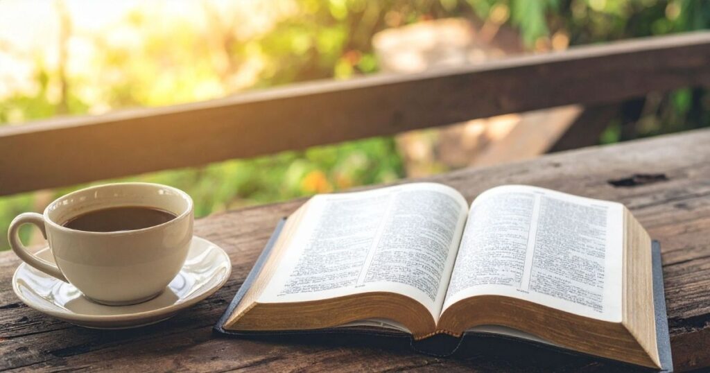 A peaceful, sunlit morning sunrise view with a warm cup of coffee sitting next to an open Bible on a rustic wooden table devotion.