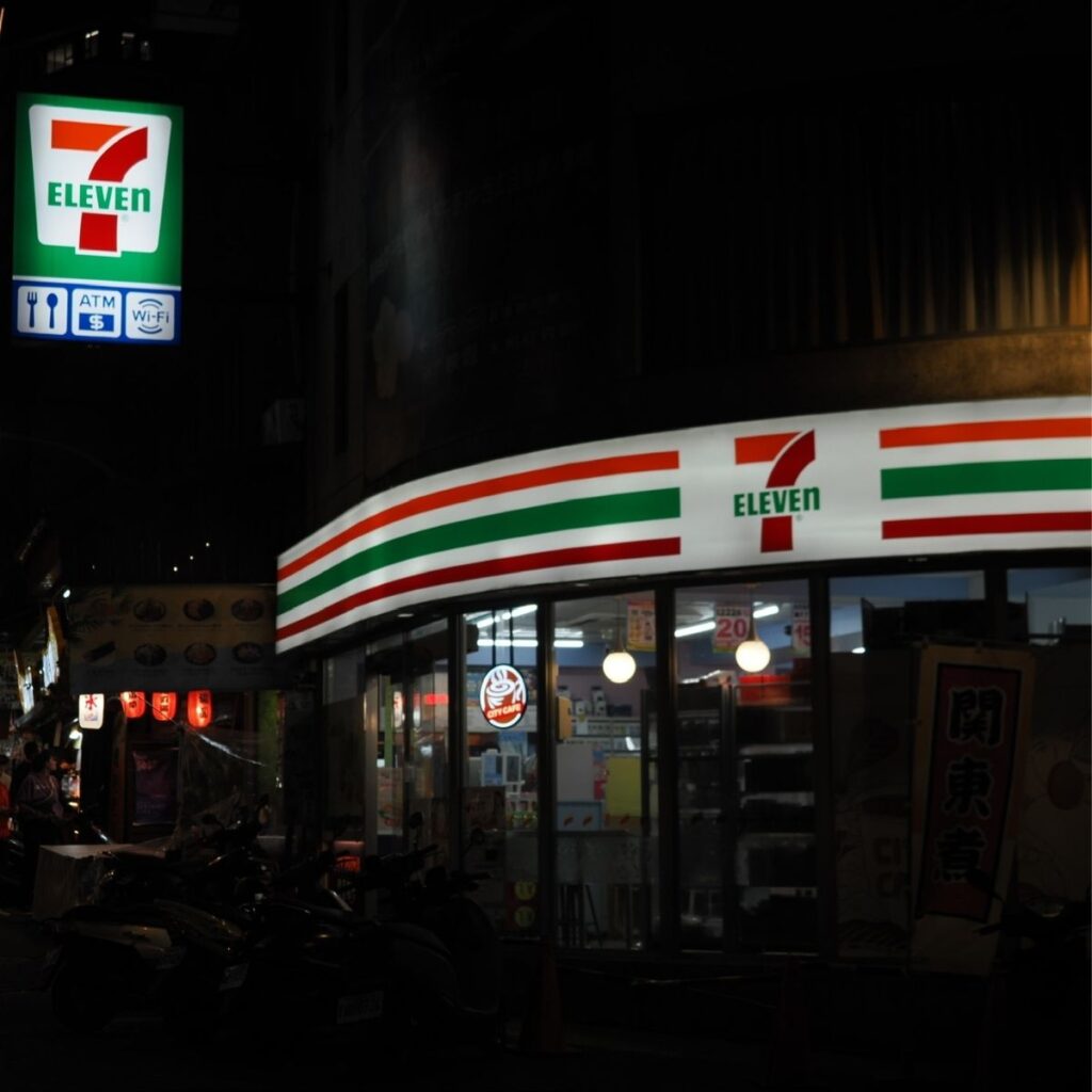 A night shot of a brightly lit 7-Eleven convenience store on a Taiwanese street corner.