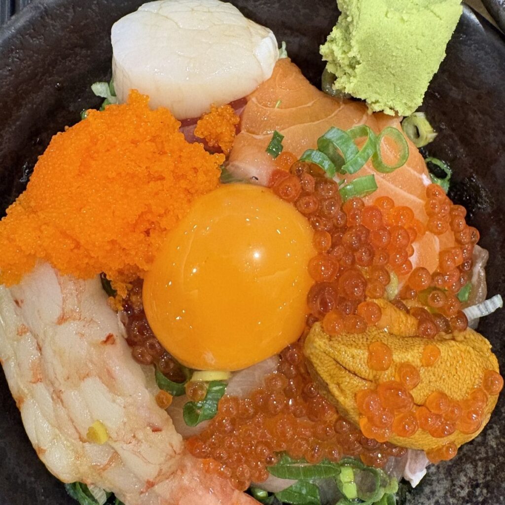 A vibrant bowl of fresh seafood sashimi slices arranged over a bed of rice.