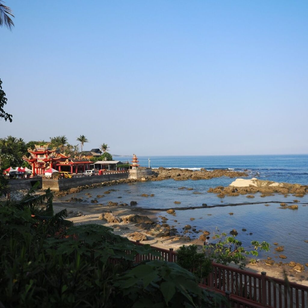 A coastal temple in Hualien overlooking a fishing village and ocean rocks at sunset.