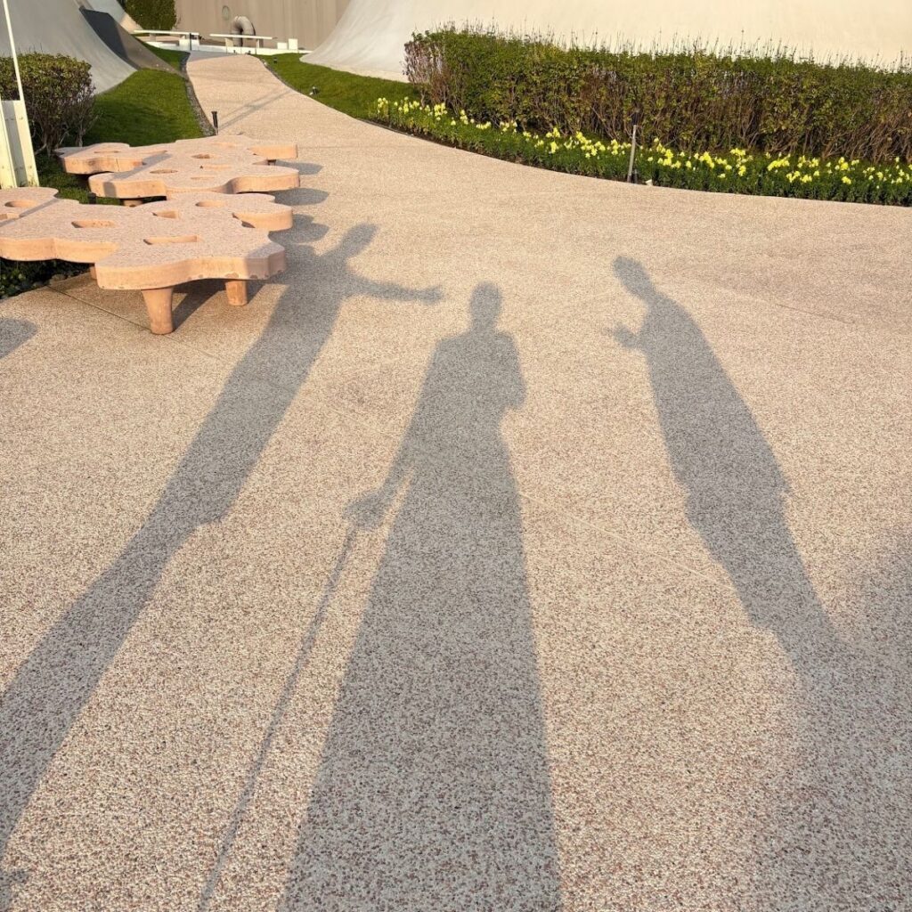 Shadows of three people cast on the modern rooftop garden of the Taichung Opera House.