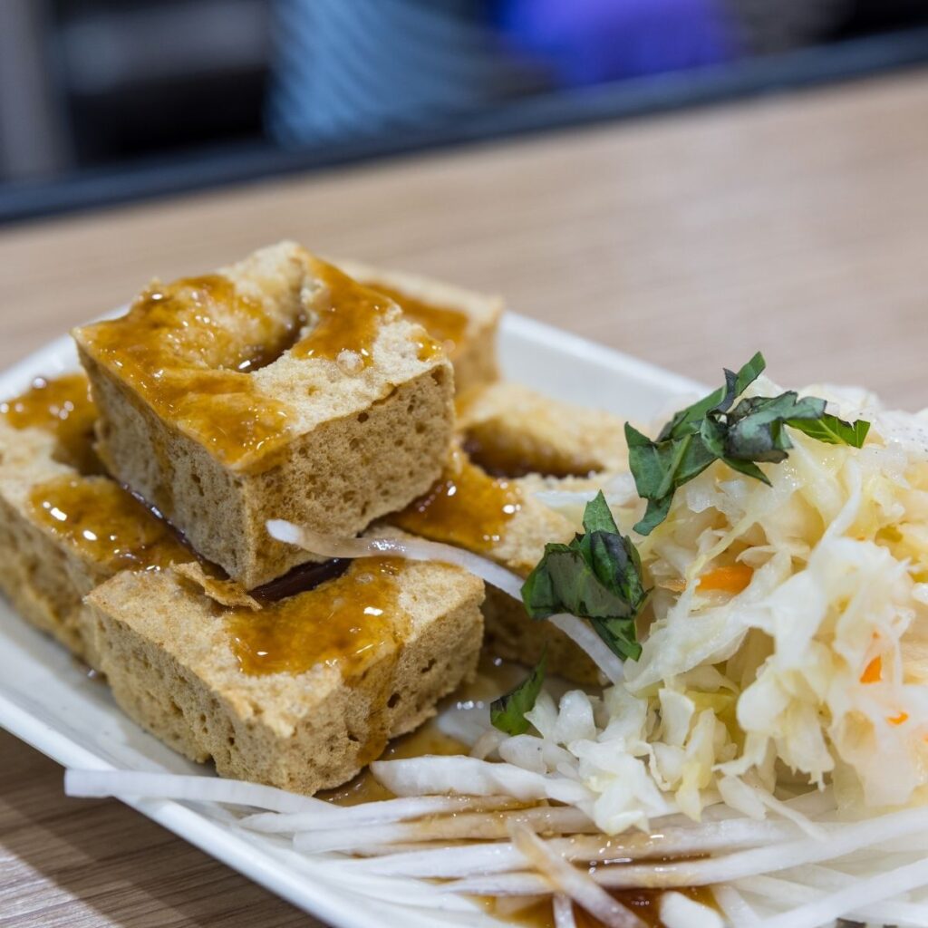 Golden, crispy stinky tofu street food served on a plate with a side of tangy pickled cabbage.