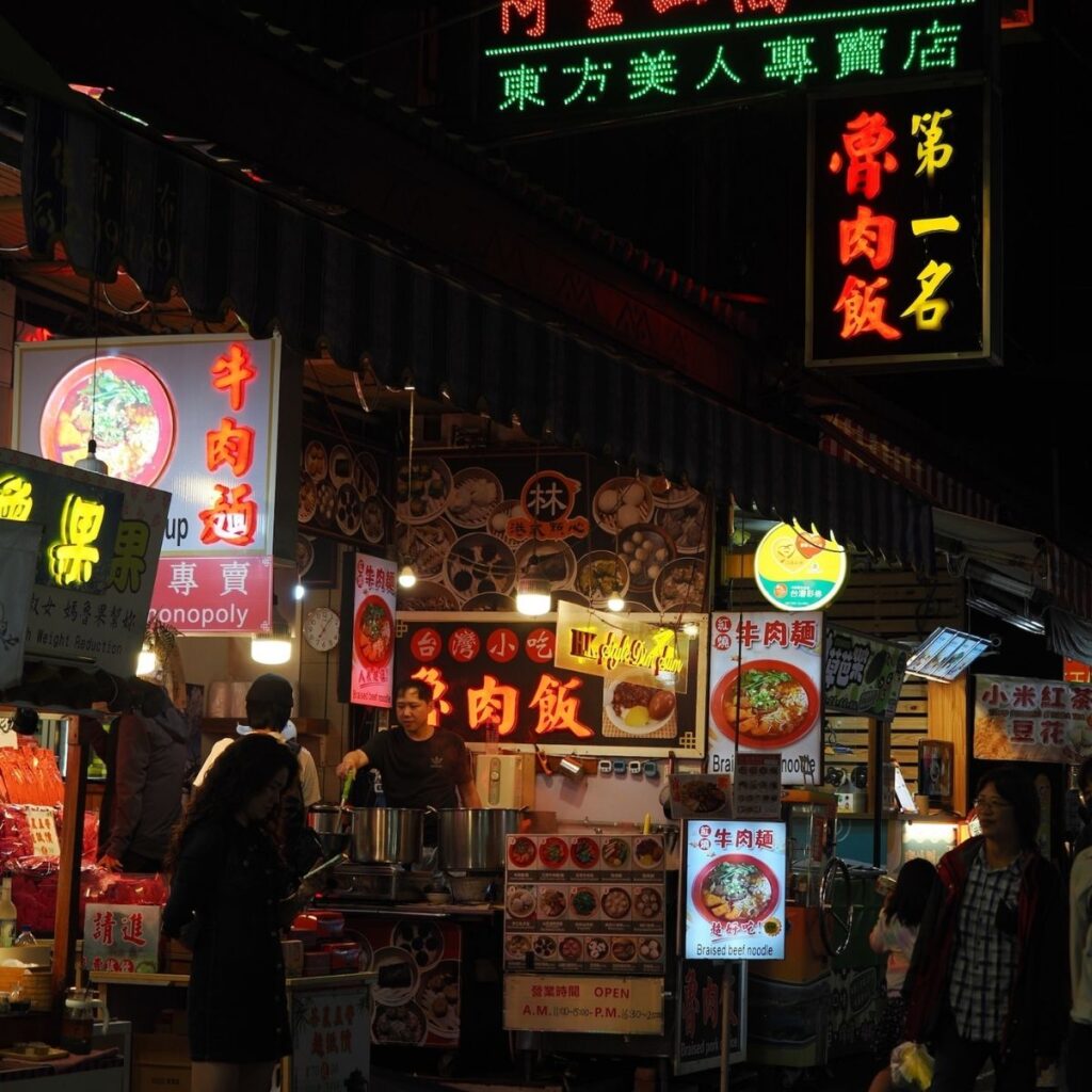A lively and bustling Taiwanese night market packed with colorful food stalls at night.