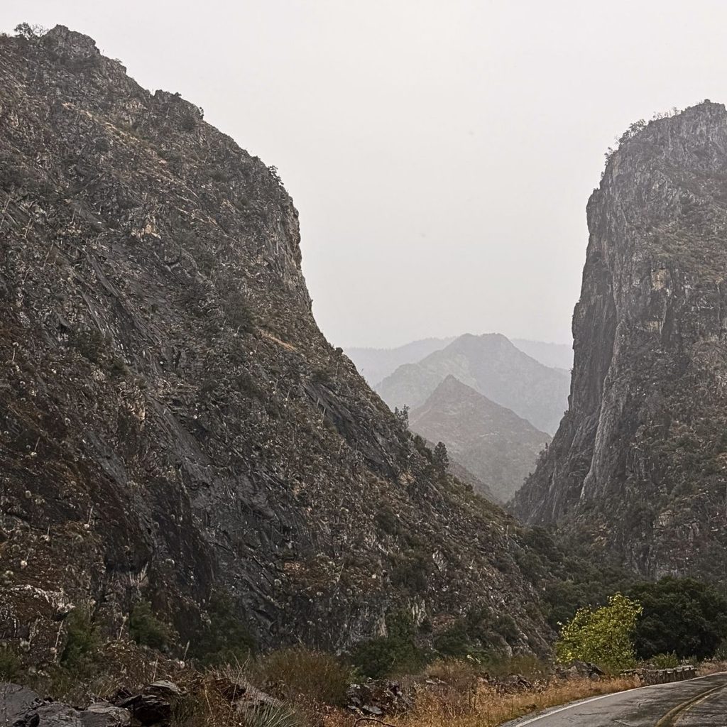 A high-altitude, misty mountain view looking deep down into the massive, steep stone walls of the Kings Canyon valley drop-off.